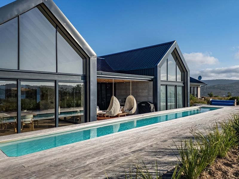 Modern architectural residence featuring a sleek lap pool, extensive timber decking, and large glass facades under a contemporary metal roof structure.