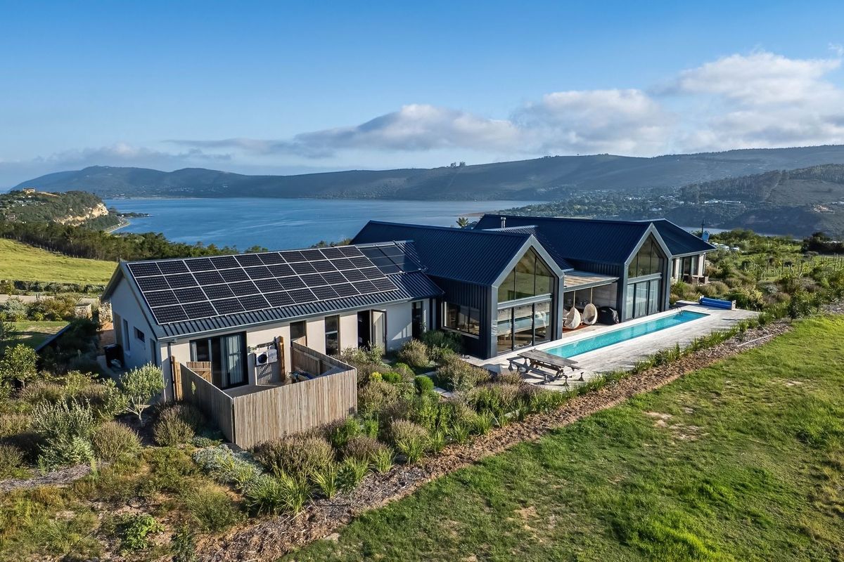 Aerial view of a modern residential property featuring a metal roof with solar panels, a swimming pool, and expansive views of the surrounding landscape.