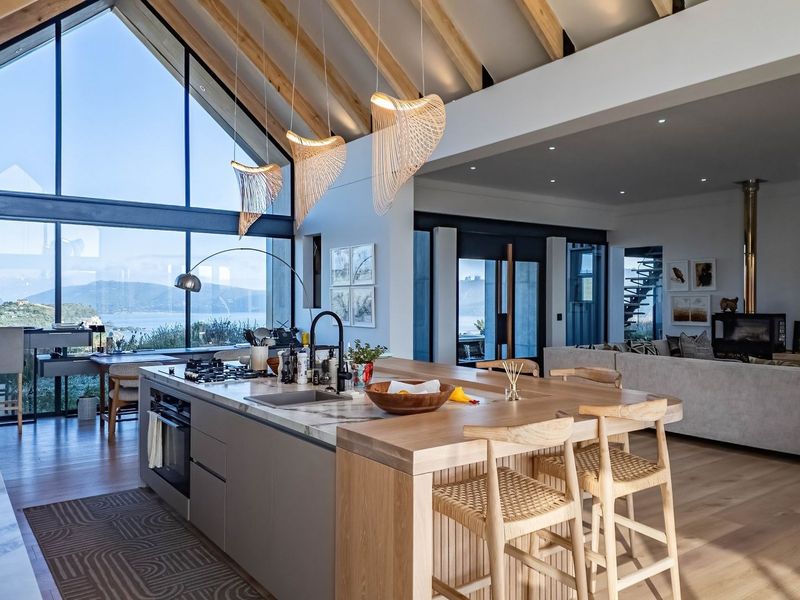 Spacious open-plan living area featuring a modern kitchen island, vaulted ceilings with exposed rafters, and expansive windows offering panoramic views.
