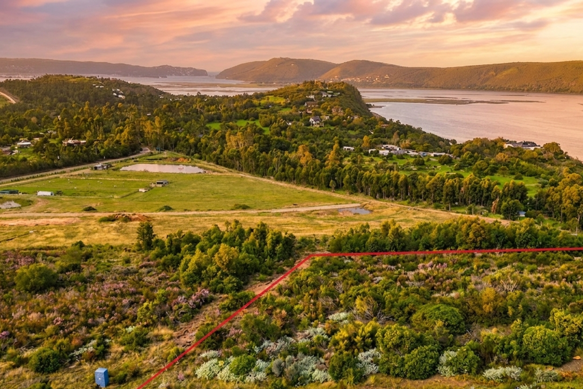 An aerial view of a vacant residential plot featuring natural vegetation, with a scenic landscape and water view in the background.