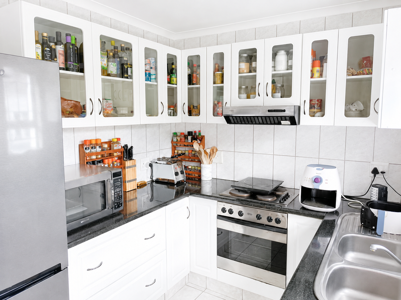 A functional kitchen featuring white cabinetry, granite countertops, a built-in oven with hob, extractor fan, and a double bowl stainless steel sink.
