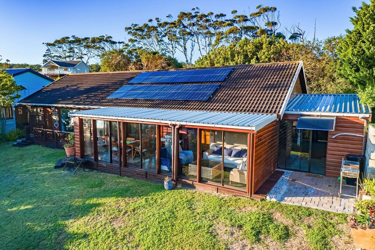 Rear view of the property featuring a tiled roof with solar panels, timber cladding, and an enclosed patio area overlooking the garden.