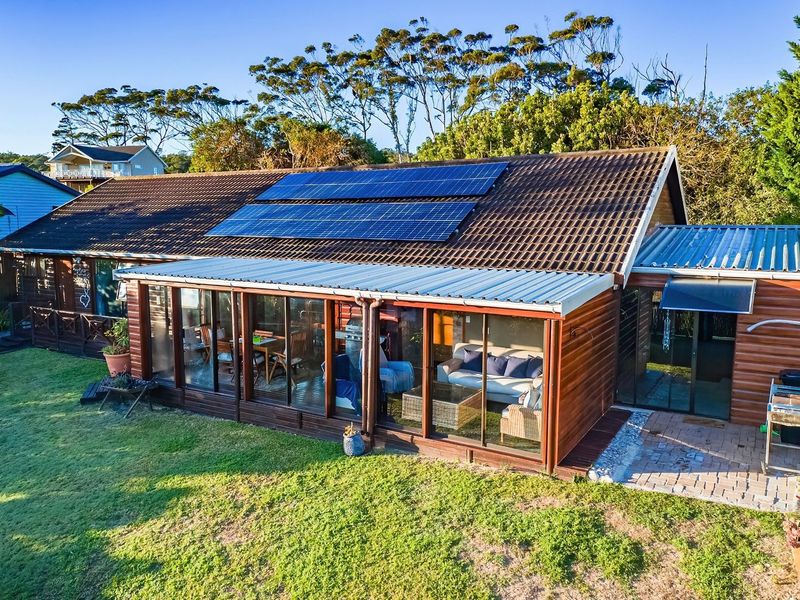 Rear view of the property featuring a tiled roof with solar panels, timber cladding, and an enclosed patio area overlooking the garden.