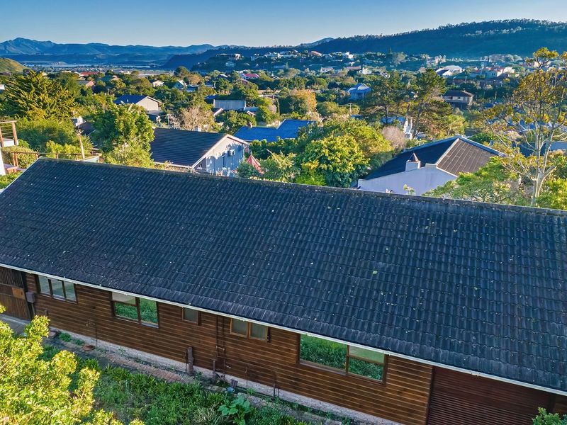 Aerial view of a residential property featuring a tiled roof, timber cladding, and an elevated timber deck overlooking the surrounding neighbourhood.