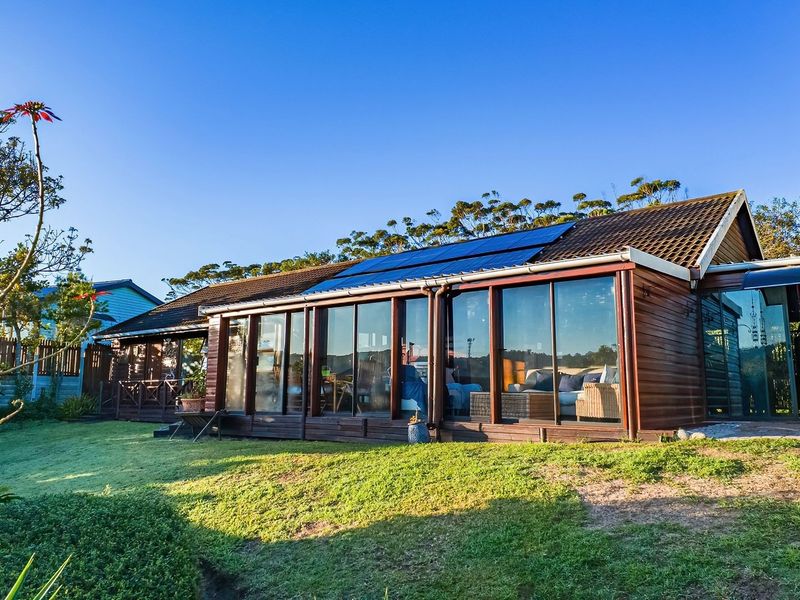 Rear view of the property featuring timber cladding, extensive sliding glass doors, and roof-mounted solar panels set against a landscaped garden.