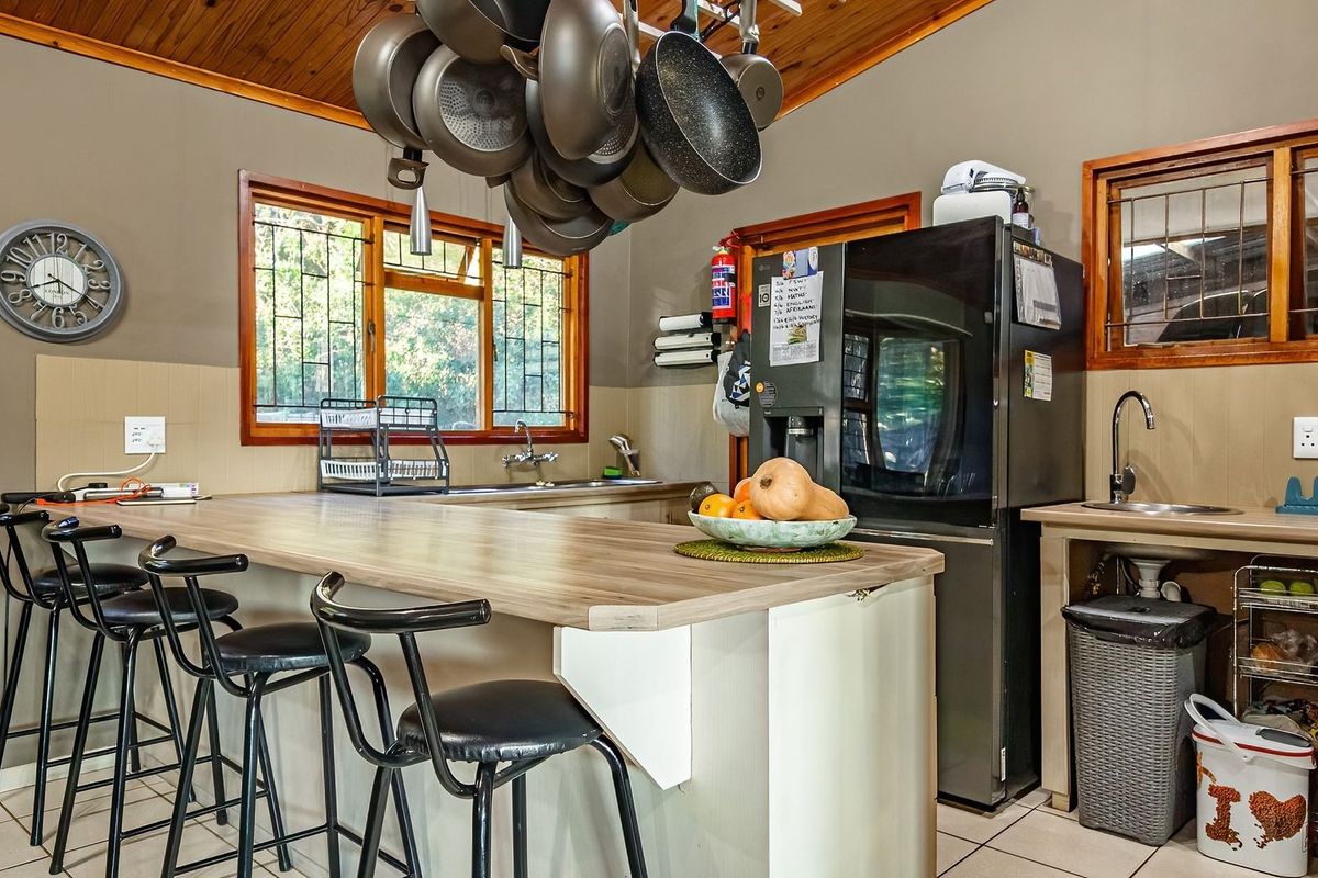 A functional kitchen featuring a breakfast bar, dual sink areas, timber ceiling accents, and tiled splashbacks with ample counter space.
