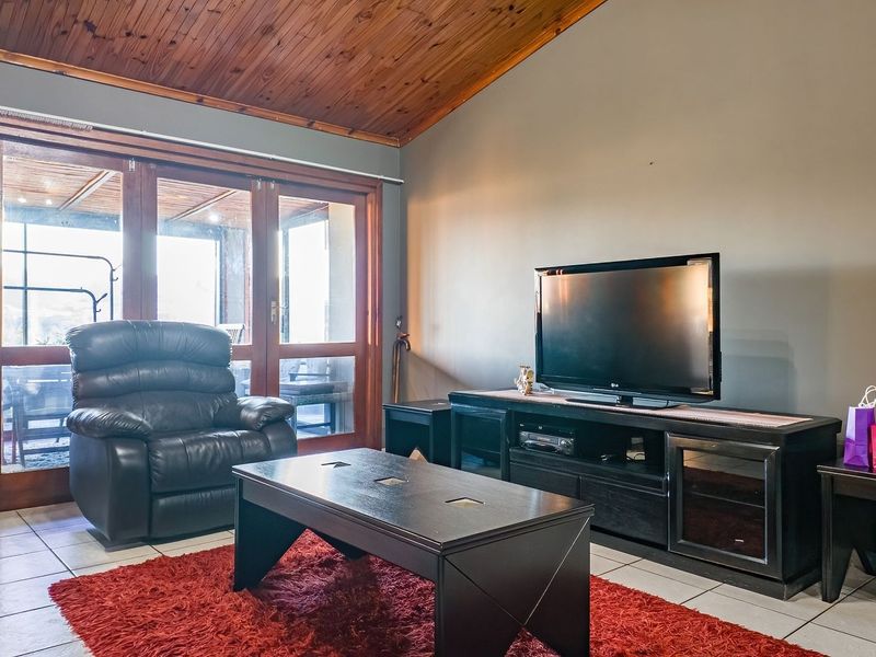 Living room featuring a raked timber ceiling, tiled flooring, and large timber-framed sliding glass doors providing access to the outdoor area.