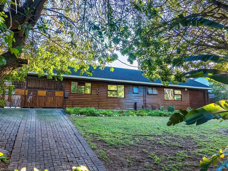 Front view of a single-story house featuring timber cladding, a tiled roof, a brick-paved driveway, and a well-maintained garden.