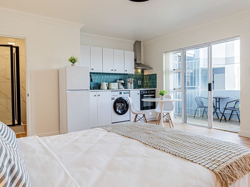 Open-plan studio apartment featuring a compact kitchen with built-in appliances, laminate flooring, and direct access to a private balcony.