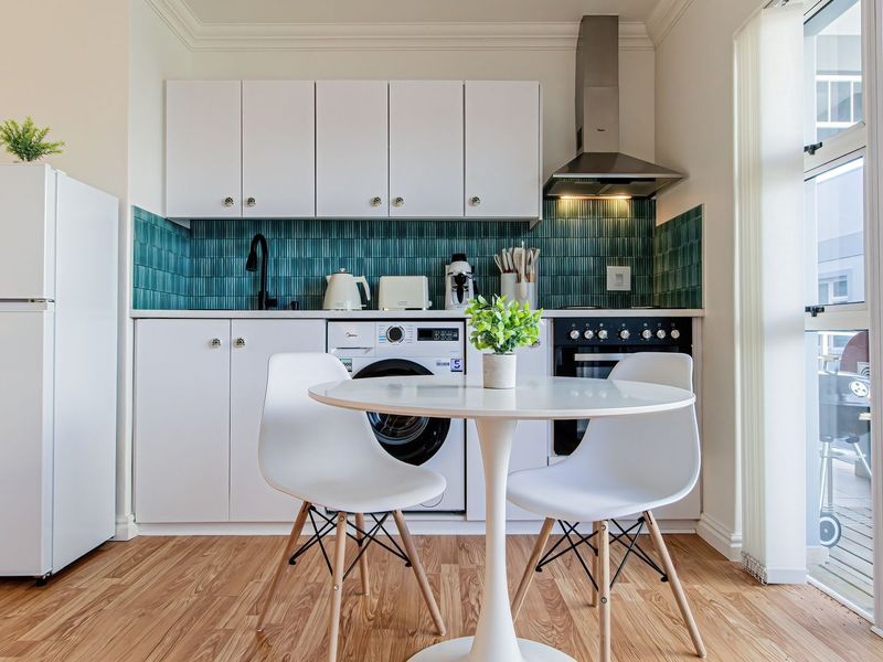 Compact modern kitchen featuring white cabinetry, a vibrant teal tiled backsplash, integrated washing machine, built-in oven, and direct access to an outdoor balcony area.