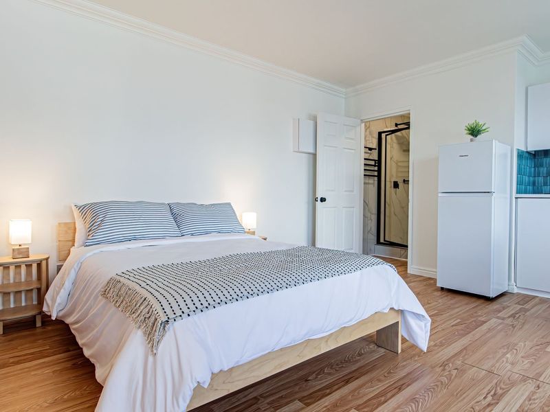 A well-maintained open-plan studio apartment featuring modern white cabinetry, a vibrant tiled backsplash, laminate flooring, and an en-suite bathroom.