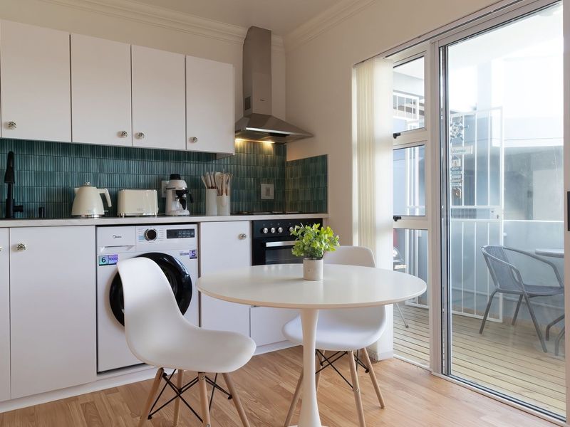 Modern open-plan kitchen featuring white cabinetry, a stylish green tiled backsplash, built-in oven, and direct access to a private balcony through sliding glass doors.