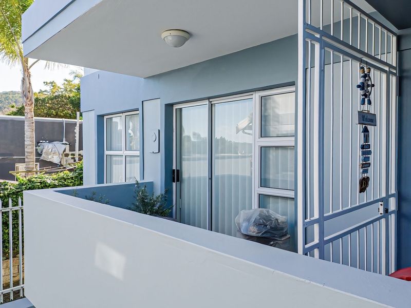A private balcony featuring a sliding glass door, secure metal gate, and concrete balustrade, providing a clean and functional outdoor space.