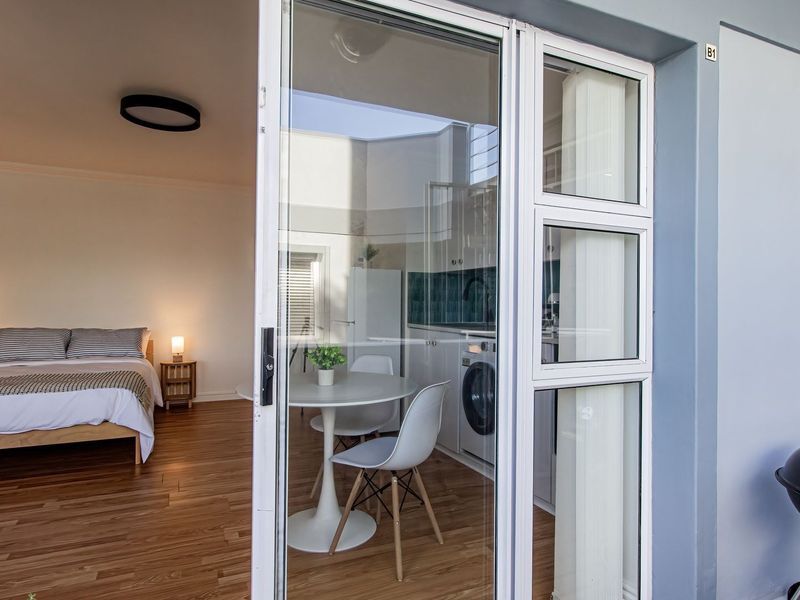 Open plan living area featuring laminate flooring and a modern kitchen with tiled backsplash, seamlessly connected to an outdoor balcony space.