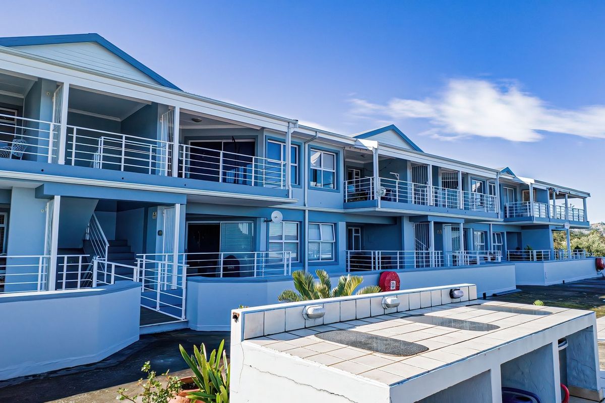 Rear elevation of a multi-story apartment complex featuring private balconies with metal railings and a communal outdoor tiled prep area.