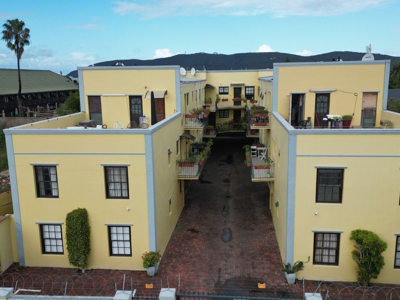 Aerial view of a multi-story apartment complex featuring yellow exterior walls, brick paved driveway, and multiple balconies.