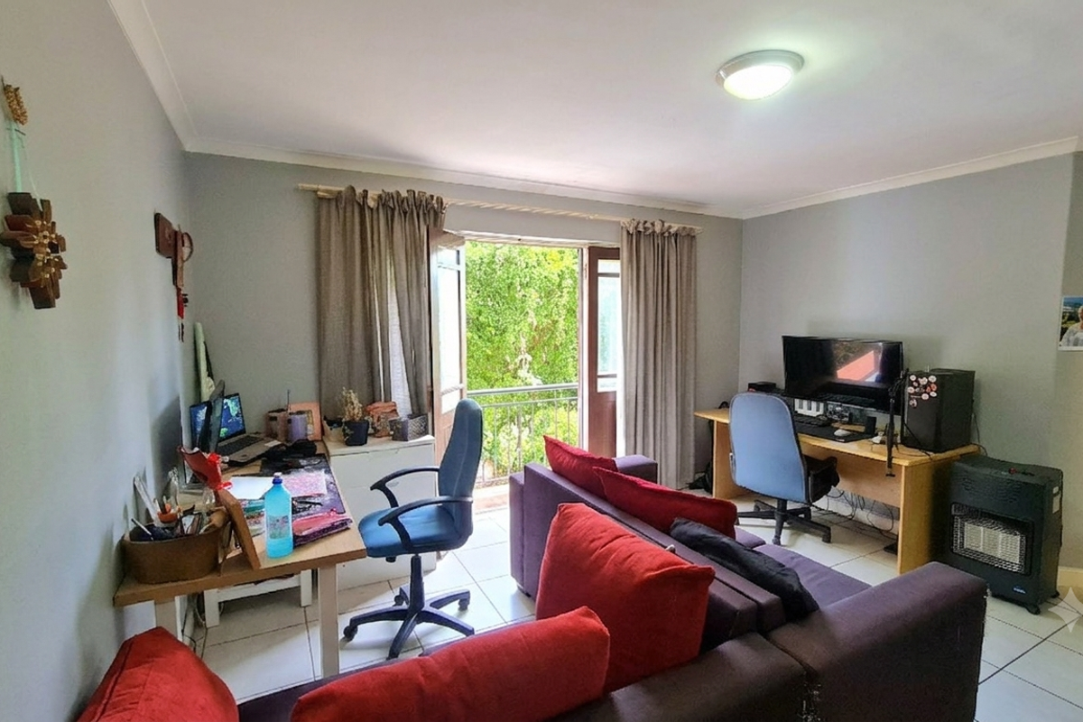 A living room area featuring tiled flooring, a ceiling light, and direct access to an outdoor balcony through a glass-paneled door.