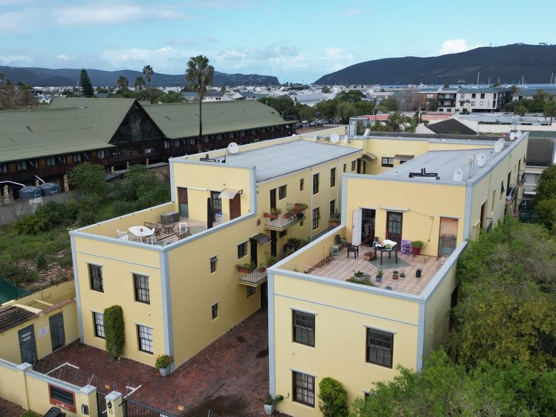 Aerial view of a multi-story apartment complex featuring flat roofs, private balconies, and a paved courtyard area in a coastal town setting.