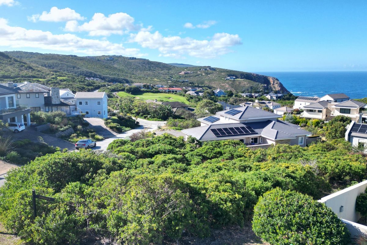 An elevated view overlooking a coastal residential estate featuring modern homes with solar panels, lush greenery, and distant ocean vistas.