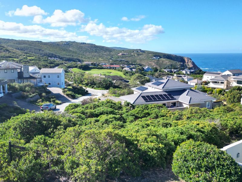 An elevated view overlooking a coastal residential estate featuring modern homes with solar panels, lush greenery, and distant ocean vistas.