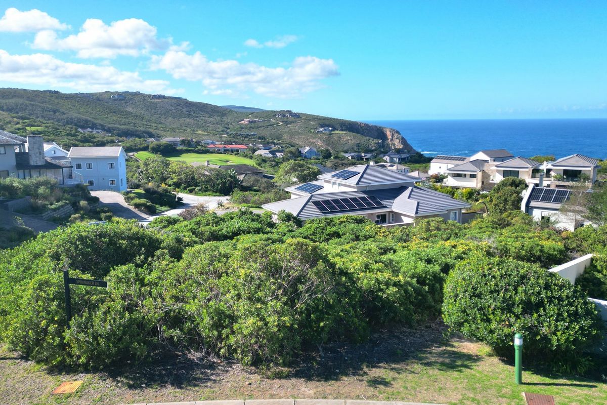 An elevated view overlooking a coastal residential estate with surrounding hills, ocean vistas, and homes featuring solar panel installations.
