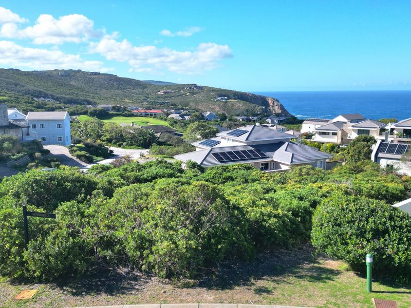 An elevated view overlooking a coastal residential estate with surrounding hills, ocean vistas, and homes featuring solar panel installations.