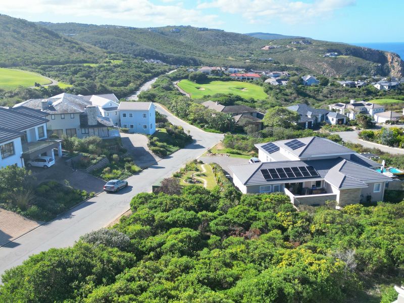 An aerial view of a residential estate featuring modern homes with tiled roofs, solar panels, and established gardens in a coastal landscape.