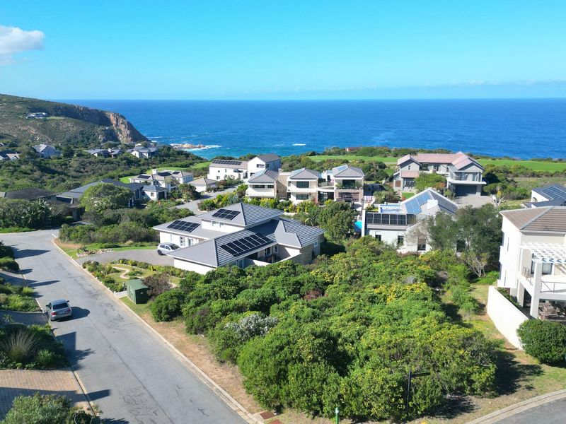 An aerial view of a coastal residential estate featuring paved roads, established vegetation, and proximity to the ocean.