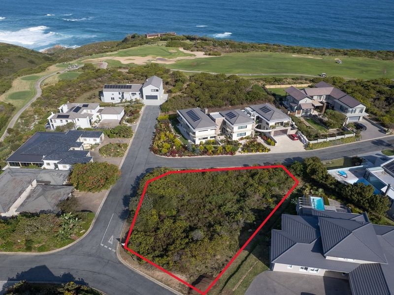 An aerial view of a vacant residential plot situated within a coastal estate, surrounded by established homes and near the coastline.
