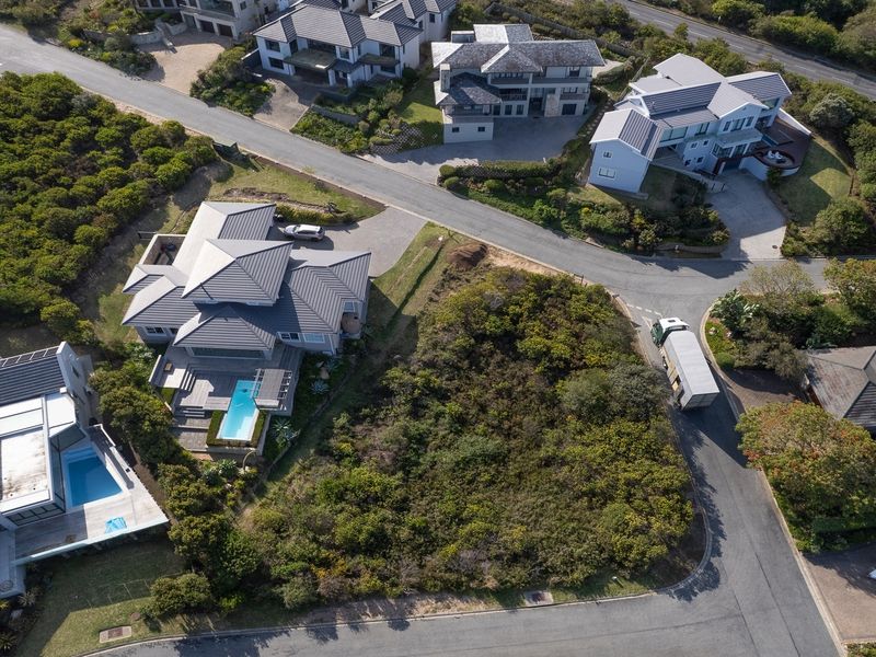 Aerial view of a vacant residential plot situated within a developed estate, featuring established road access and surrounding luxury homes.