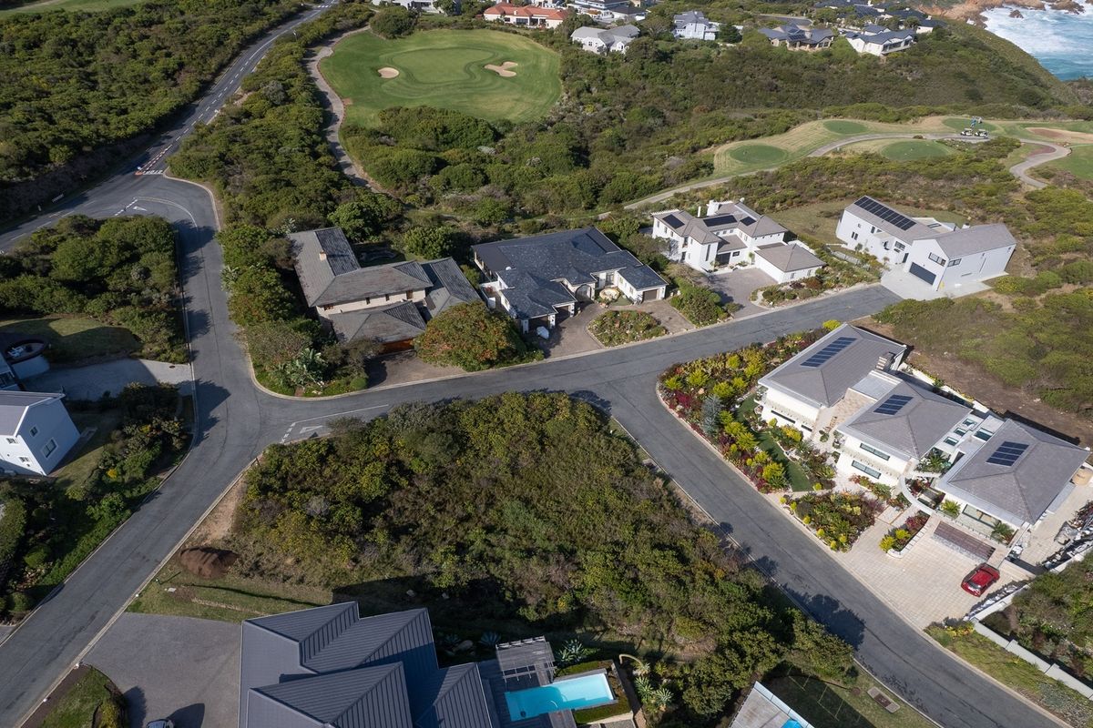 An aerial view of a residential estate featuring paved roads, established homes, and proximity to a golf course and the coastline.