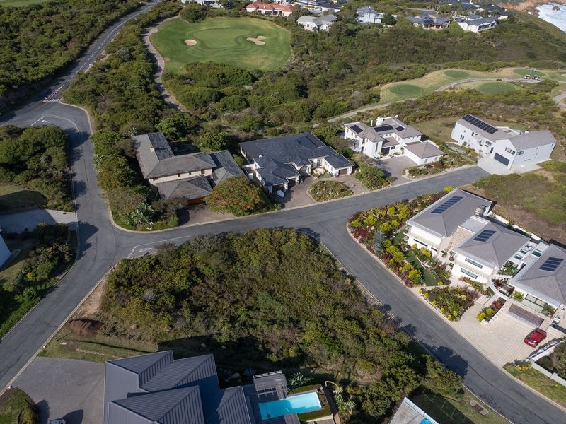 An aerial view of a residential estate featuring paved roads, established homes, and proximity to a golf course and the coastline.