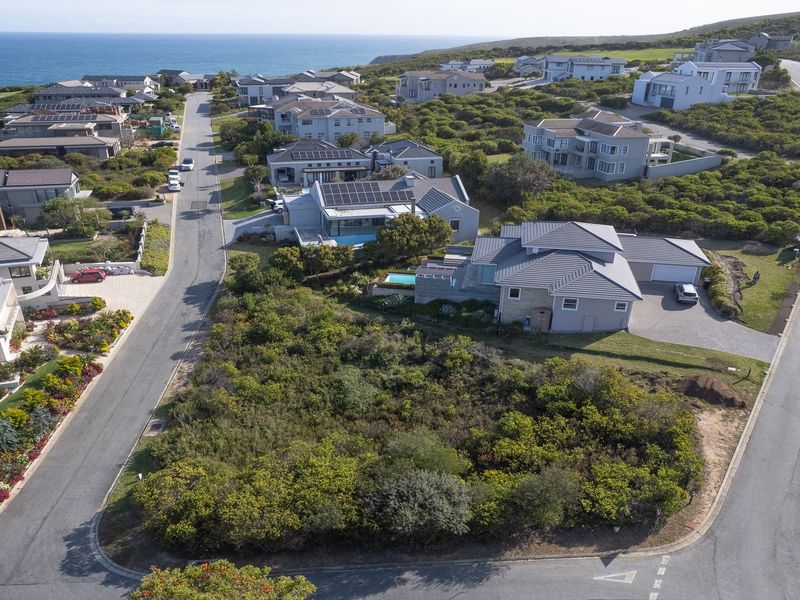 An aerial view of a vacant residential plot situated in a coastal estate, surrounded by established homes and natural vegetation.