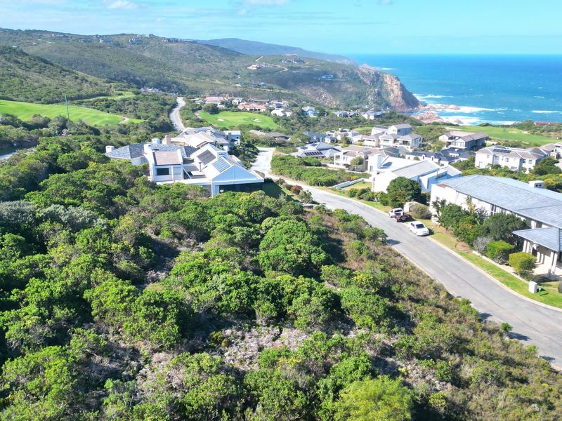 An aerial view of a residential estate featuring coastal landscape, established road infrastructure, and surrounding homes near the ocean.