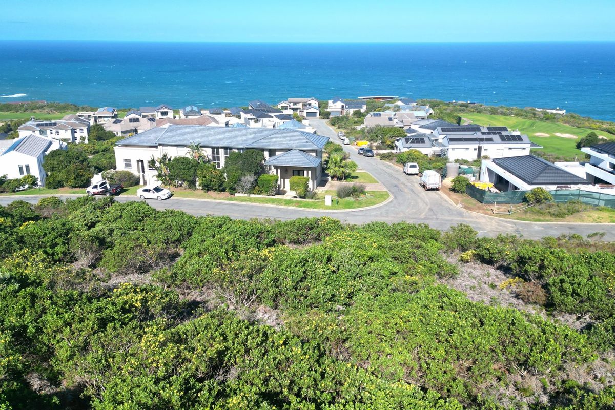 An aerial view of a coastal residential estate featuring established homes, paved streets, and surrounding natural vegetation overlooking the ocean.