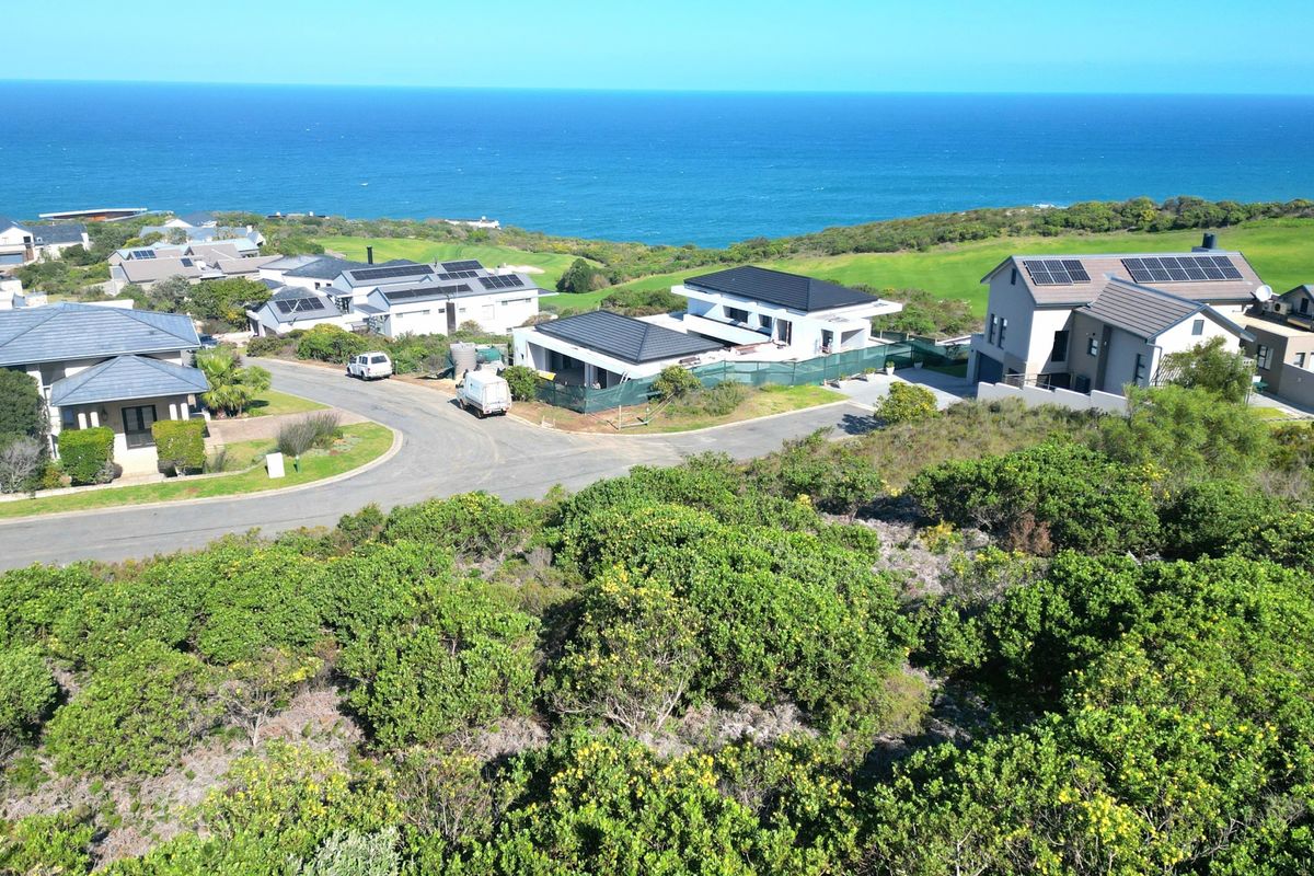 An aerial view of a residential estate featuring paved roads and coastal landscape, showcasing the surrounding neighborhood and proximity to the ocean.