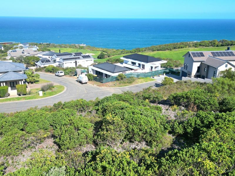 An aerial view of a residential estate featuring paved roads and coastal landscape, showcasing the surrounding neighborhood and proximity to the ocean.