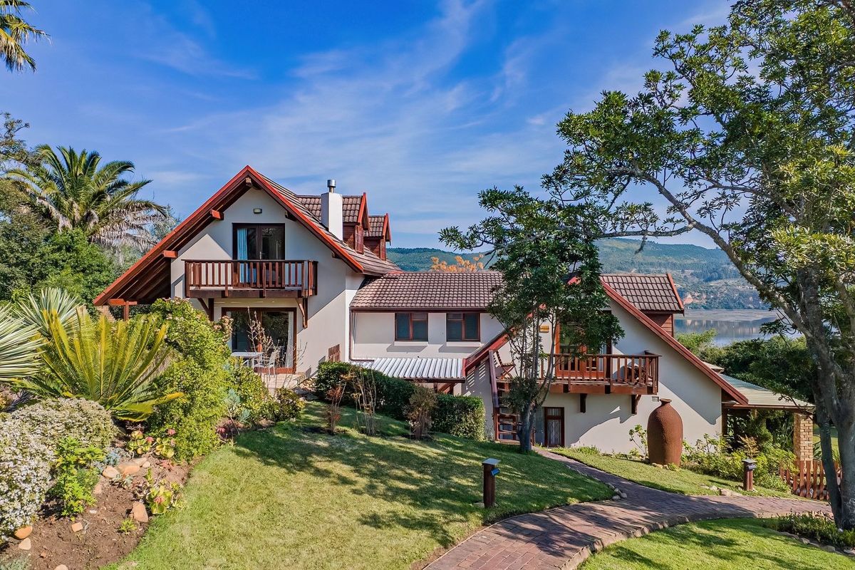 Rear view of the lodge featuring timber balconies, a well-maintained garden, and a brick pathway leading towards the property with scenic landscape views.