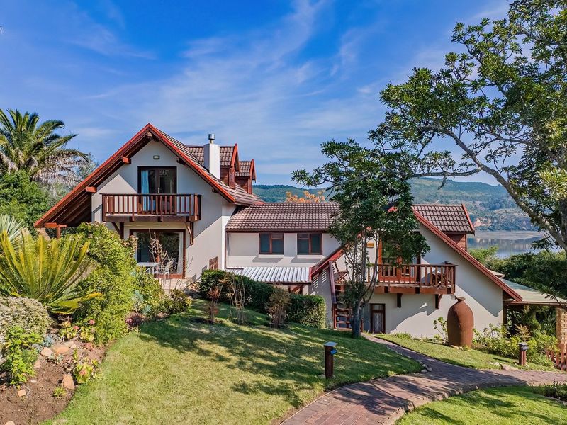 Rear view of the lodge featuring timber balconies, a well-maintained garden, and a brick pathway leading towards the property with scenic landscape views.