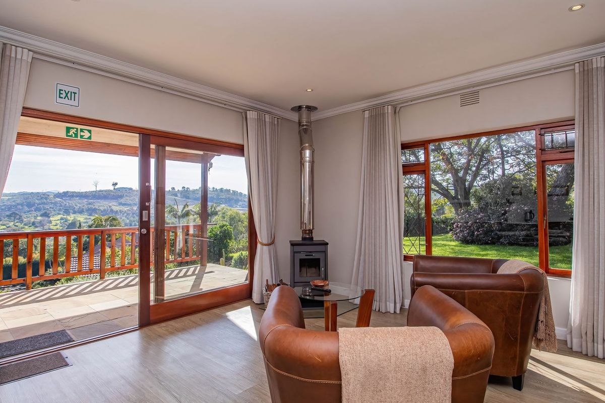 A bright living room featuring a wood-burning fireplace, large sliding doors opening to a wooden deck, and expansive views of the surrounding landscape.