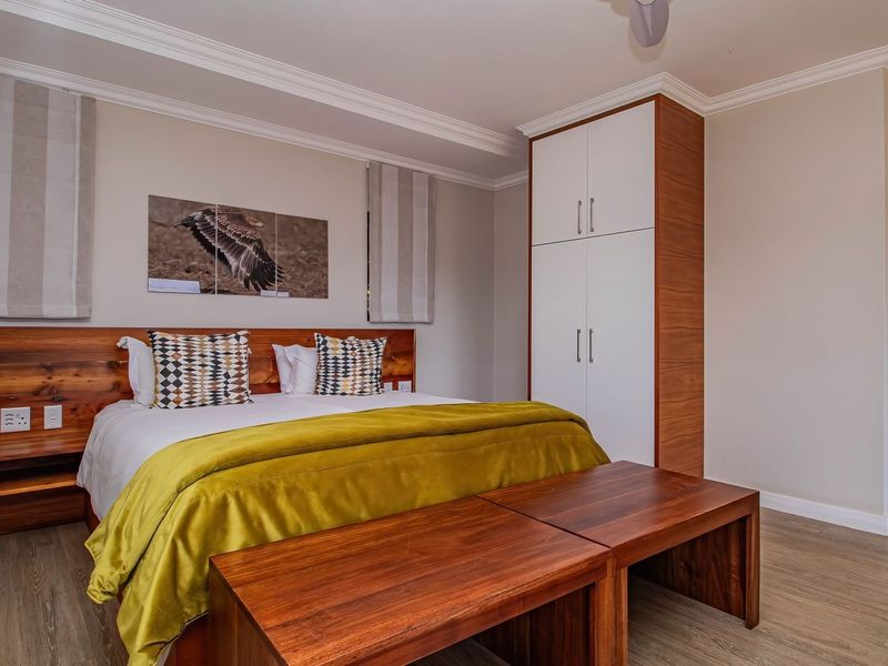A well-maintained bedroom featuring built-in wooden wardrobes, crown molding, and laminate flooring, with an en-suite bathroom visible through the doorway.