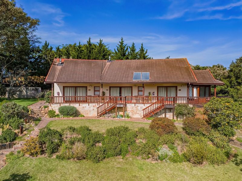 Rear view of a lodge featuring a tiled roof with solar panels, a raised timber deck with stairs, and extensive landscaped gardens.
