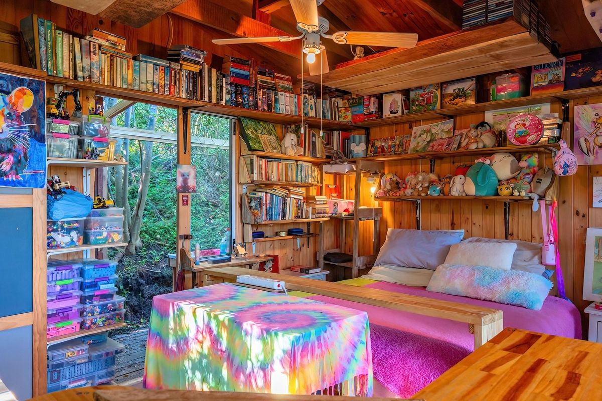 A cozy bedroom featuring warm timber wall cladding, exposed ceiling beams, a ceiling fan, and extensive built-in shelving with direct access to the outdoors.