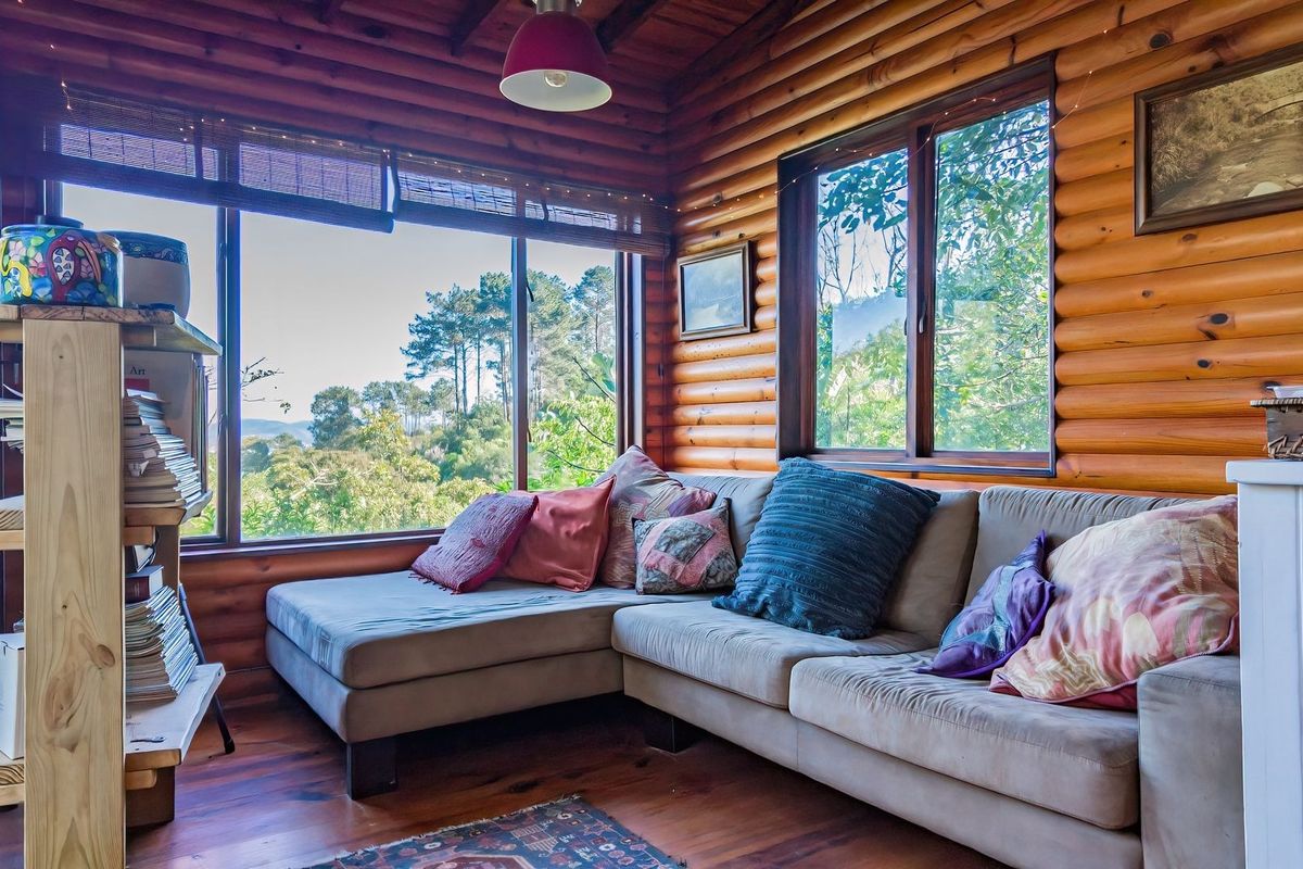 A cozy living room featuring rustic log cabin walls, warm timber flooring, and large windows that provide ample natural light and scenic views.