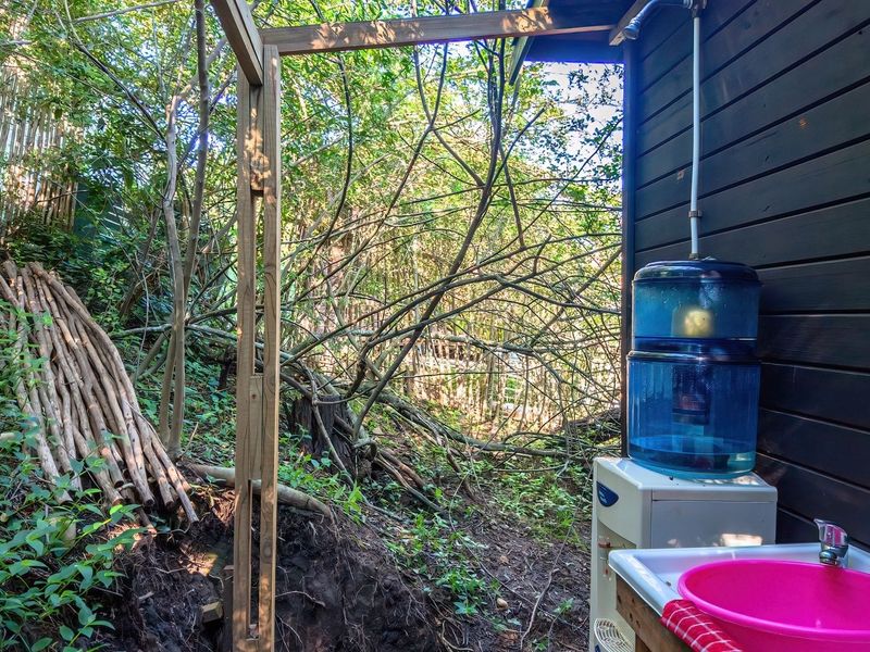 An outdoor utility area featuring a basic shower setup and sink attached to the exterior timber wall of the property.