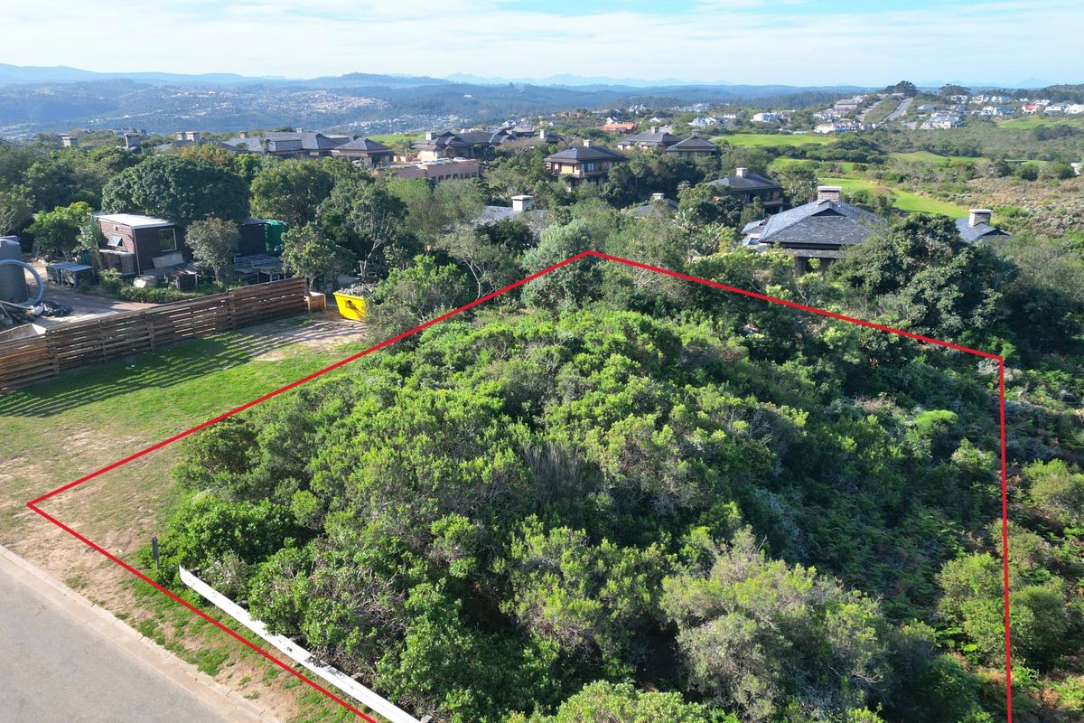 An aerial view of a vacant residential plot featuring dense natural vegetation, situated within a developed estate with surrounding homes.