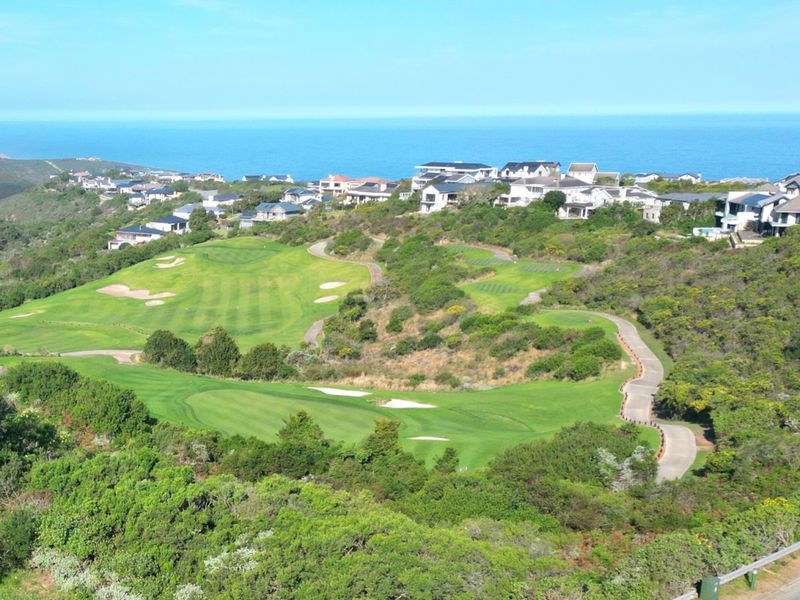An elevated aerial view of a coastal golf course estate, showcasing manicured fairways, surrounding natural vegetation, and proximity to the ocean.