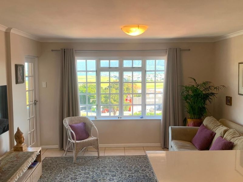 A bright living room featuring tiled flooring, coving, and a large multi-pane window offering scenic views.