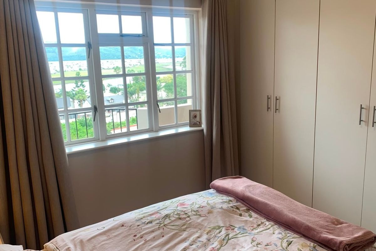 A well-maintained bedroom featuring built-in cupboards and a large multi-pane window offering scenic views.