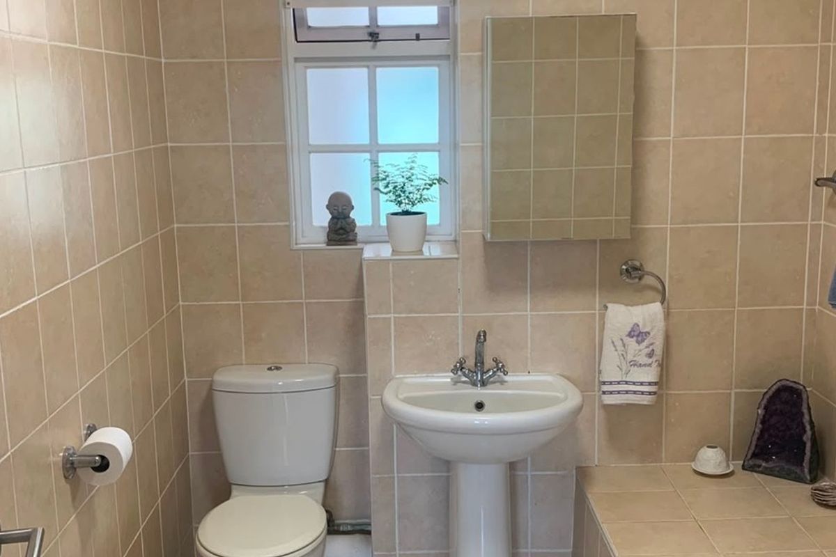 A functional bathroom featuring tiled walls and flooring, a pedestal washbasin, a toilet, and a built-in medicine cabinet.